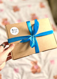 Hand holding a ready wrapped daddy to be box that has blue ribbon wrapped around with it and has a bow. In left corner has a sticker that says "just for you". Letterbox A5 sized box.